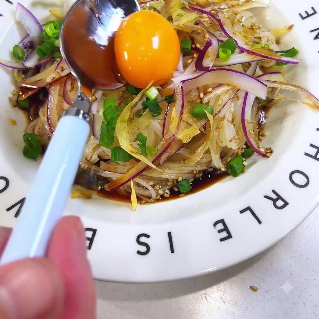 Un tuorlo duovo crudo e brillante poggiato su un cucchiaio posizionato al centro dei noodles somen conditi.