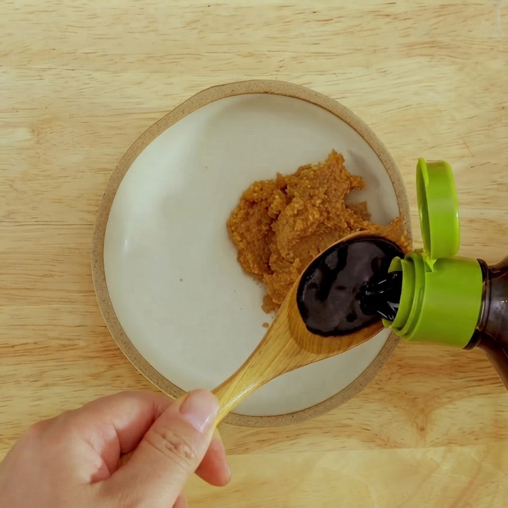 Salsa di soia scura versata in una ciotola con pasta di miso rosso densa.