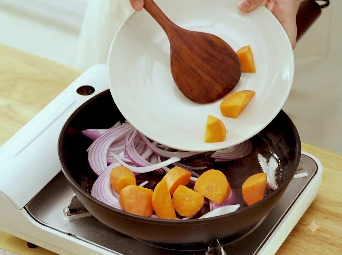 Pezzi di carota cruda aggiunti da un piatto in una padella con cipolle saltate.