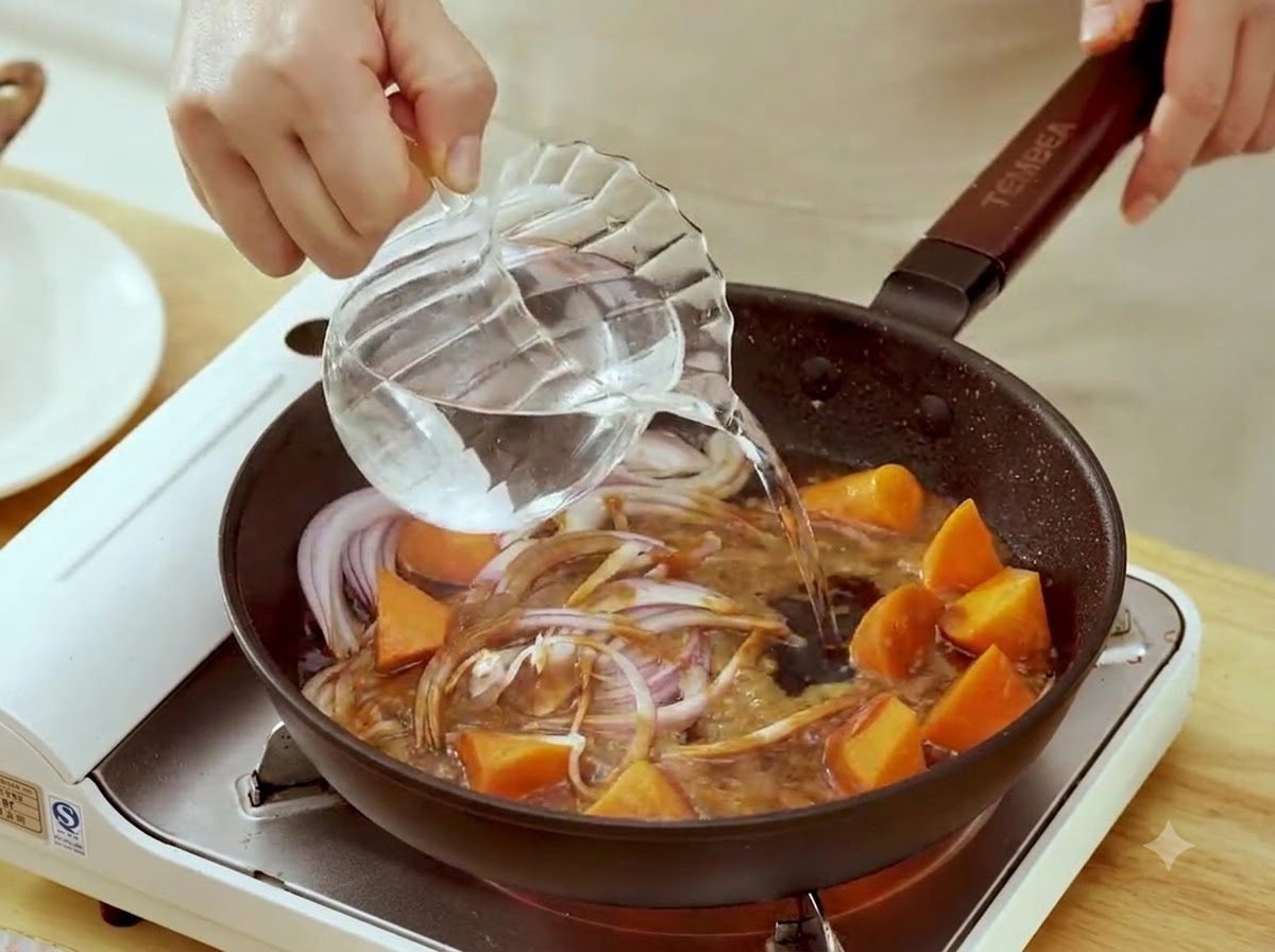 Acqua versata da una brocca in una padella con cipolle e carote nella salsa al miso.