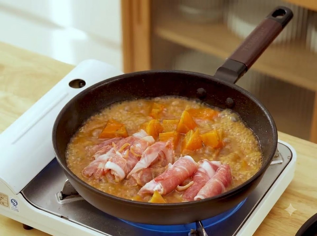 Fette di manzo arrotolate crude disposte in padella con brodo bruno al miso e pezzi di carota.