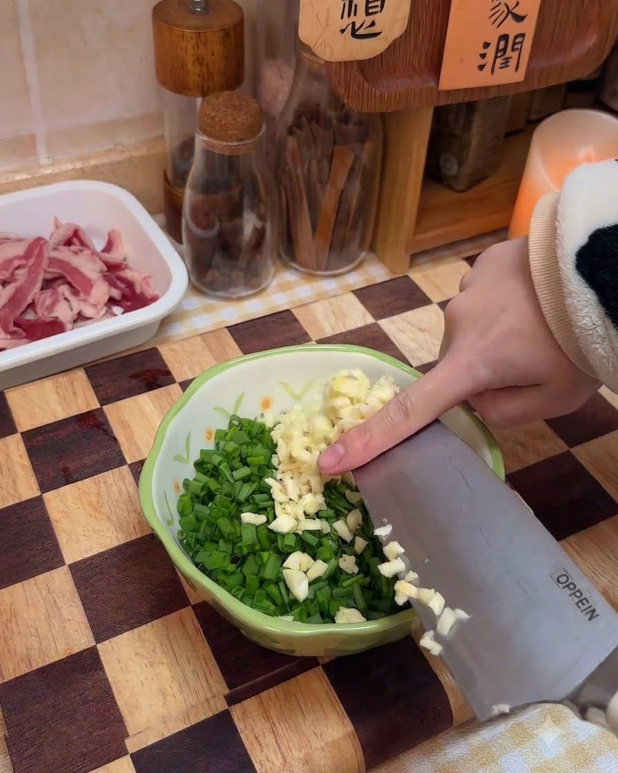 Aglio tritato aggiunto in una ciotola contenente cipollotti tritati e spezie.