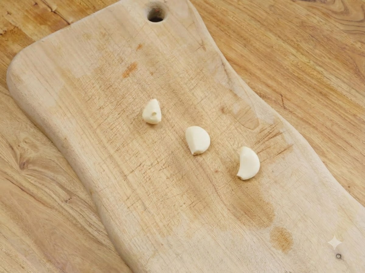 Tre spicchi daglio pelati appoggiati su un tagliere di legno.