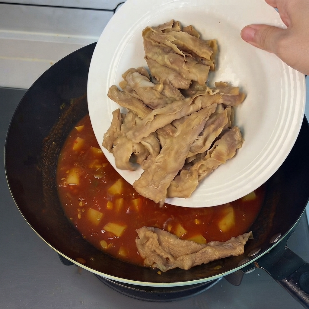 Rotoli di manzo pre-sbollentati fatti scivolare da un piatto bianco nel brodo rosso saporito nel wok.