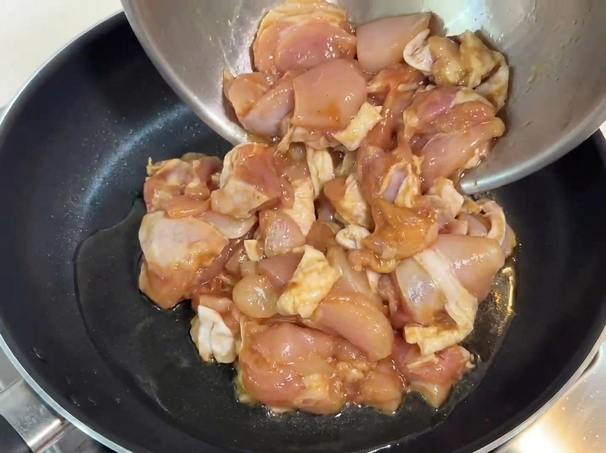 Pezzi di pollo marinato versati in una padella con olio caldo.