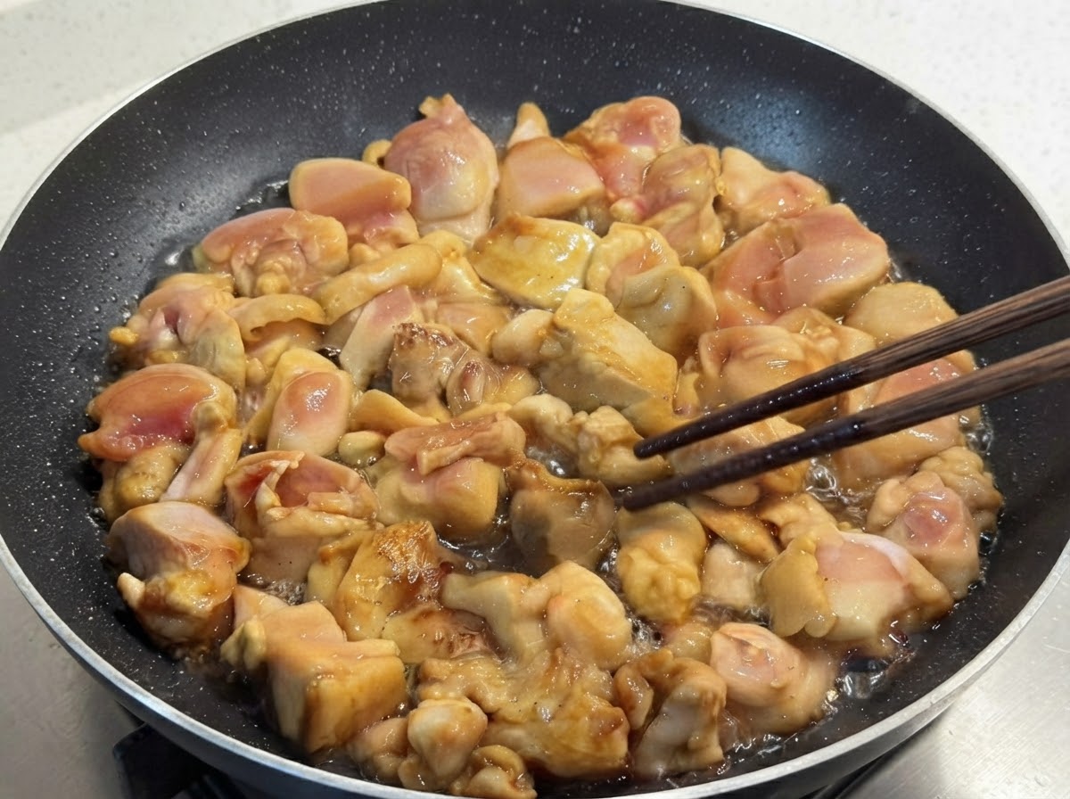 Pezzi di pollo marinato saltati in una padella e girati con cura usando bacchette di legno.