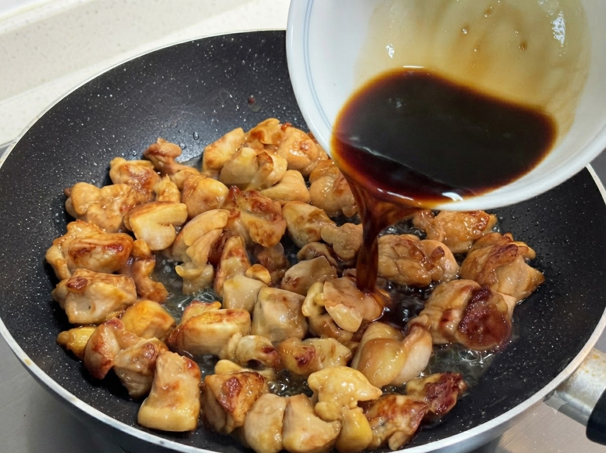 Una miscela di salsa scura e saporita versata da una ciotola bianca sopra pezzi di pollo dorati saltati in padella.