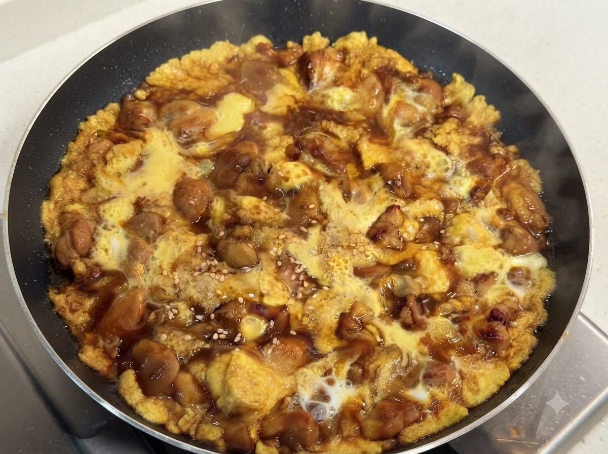 Una padella calda piena di tenero pollo cotto e uovo vellutato in una saporita salsa scura, guarnita con semi di sesamo bianco.