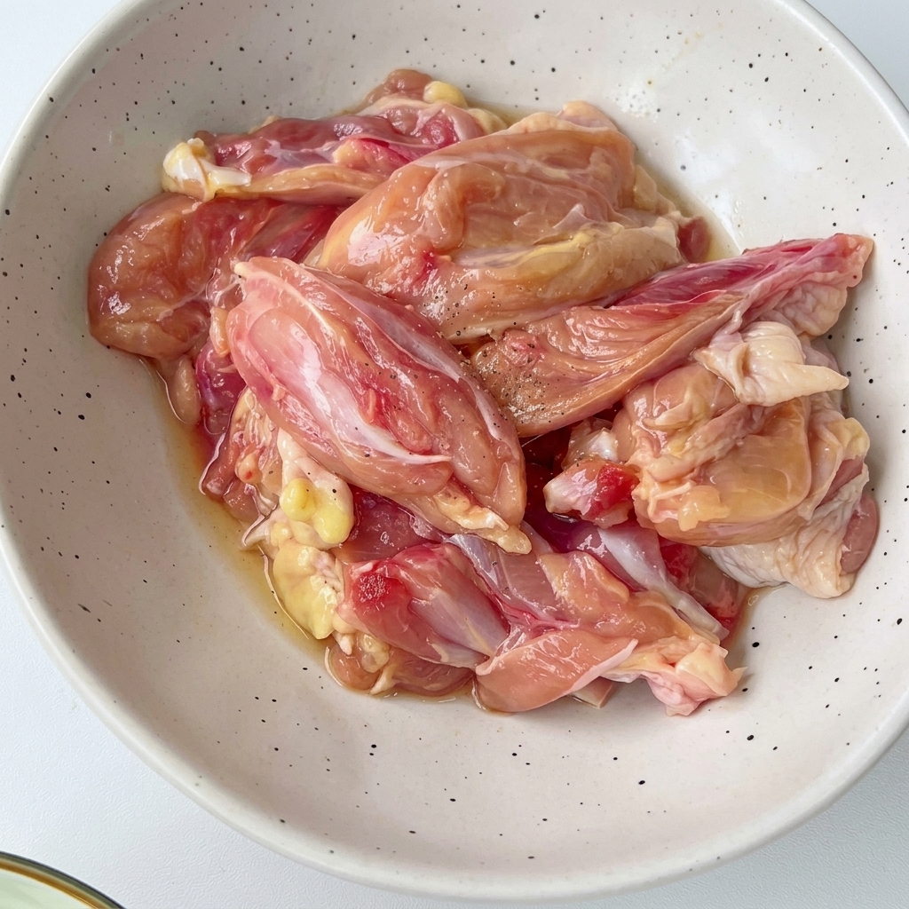 Pezzi di pollo tagliati allinterno di una ciotola bianca maculata mescolati con condimenti e aromi.