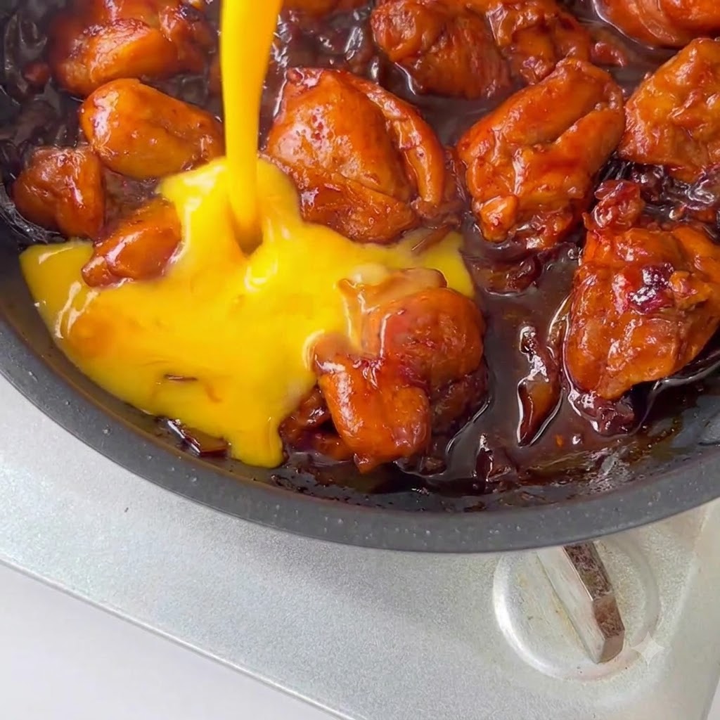 Uova sbattute versate sopra il pollo e la salsa in una padella.