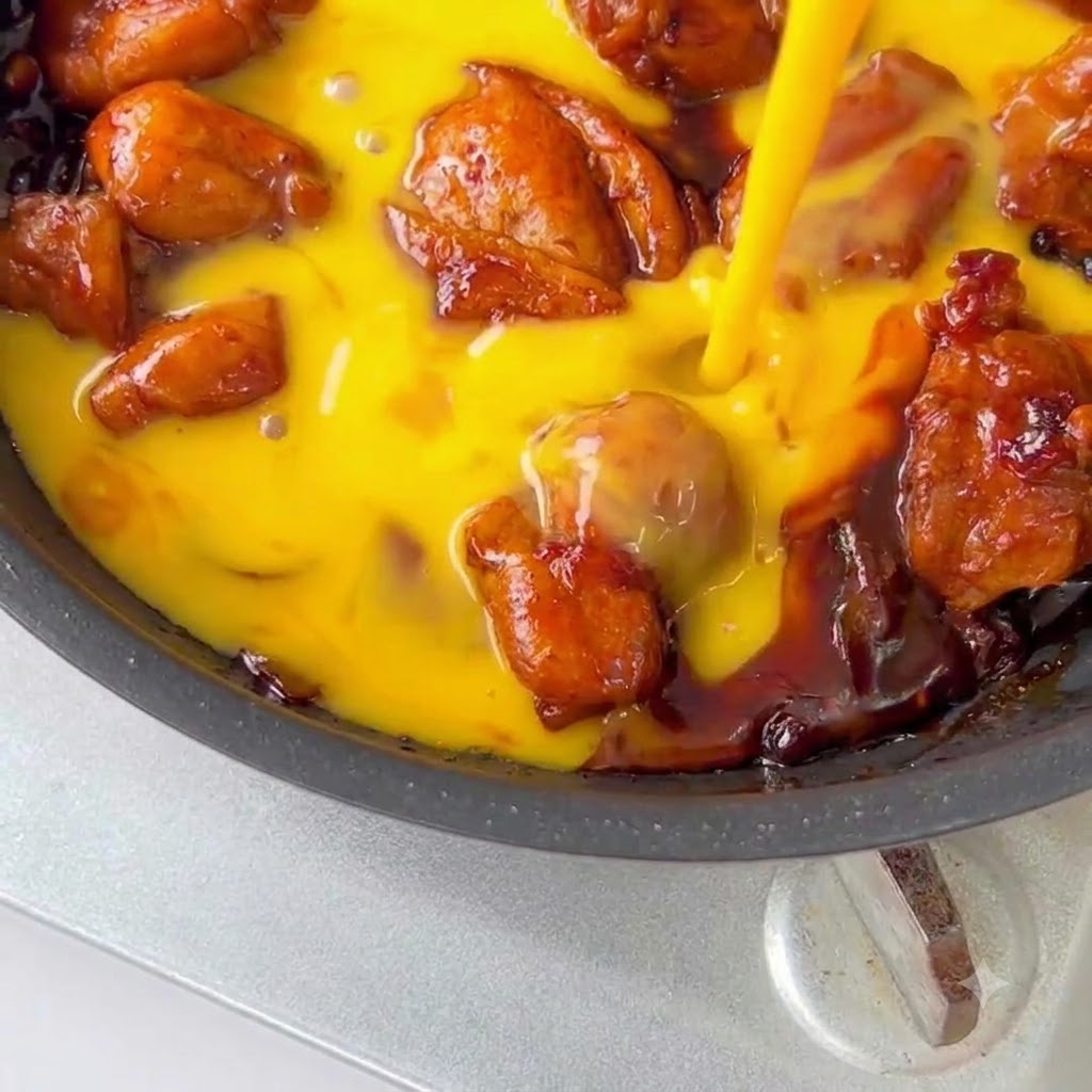 Composto di pollo e uova guarnito con semi di sesamo e cipollotti verdi in padella.