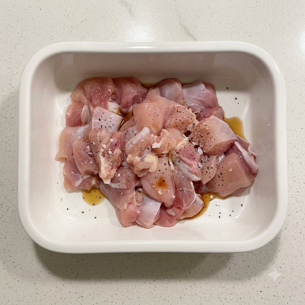 Pezzi di pollo crudo conditi con amido, salsa di soia e pepe nero allinterno di un contenitore di ceramica bianca.