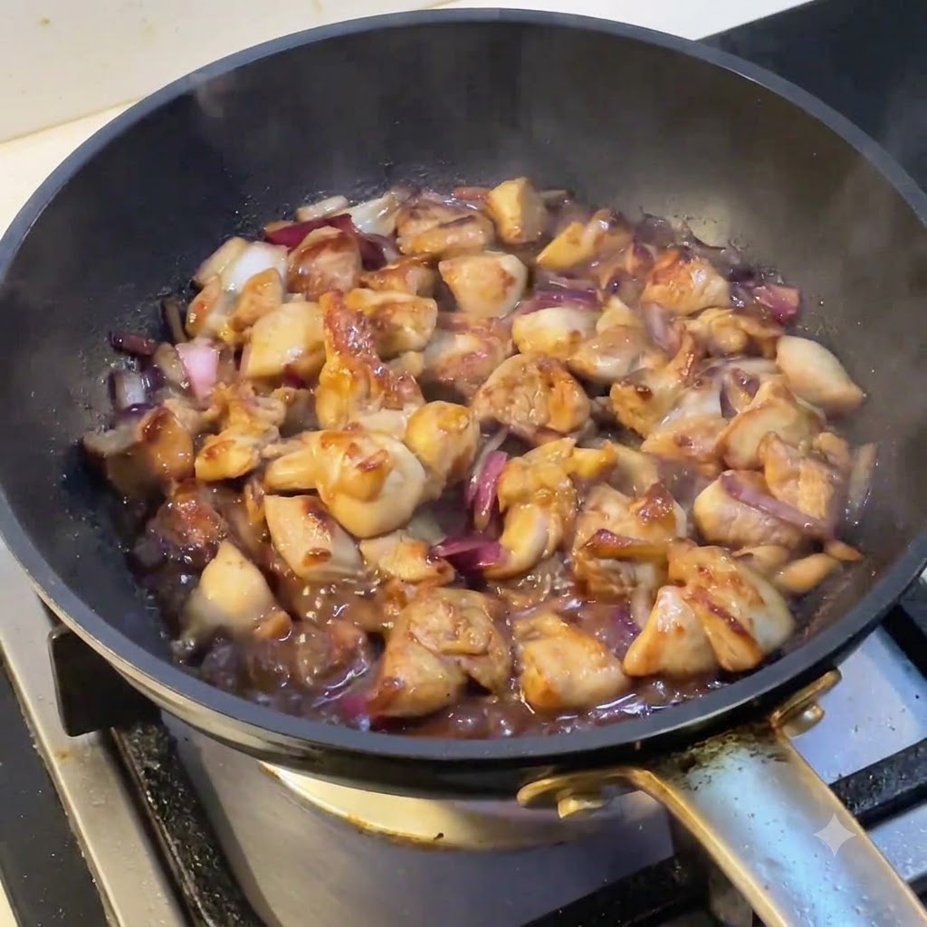 Una padella piena di pollo e cipolle in ebollizione mentre il vapore sale dalla superficie.