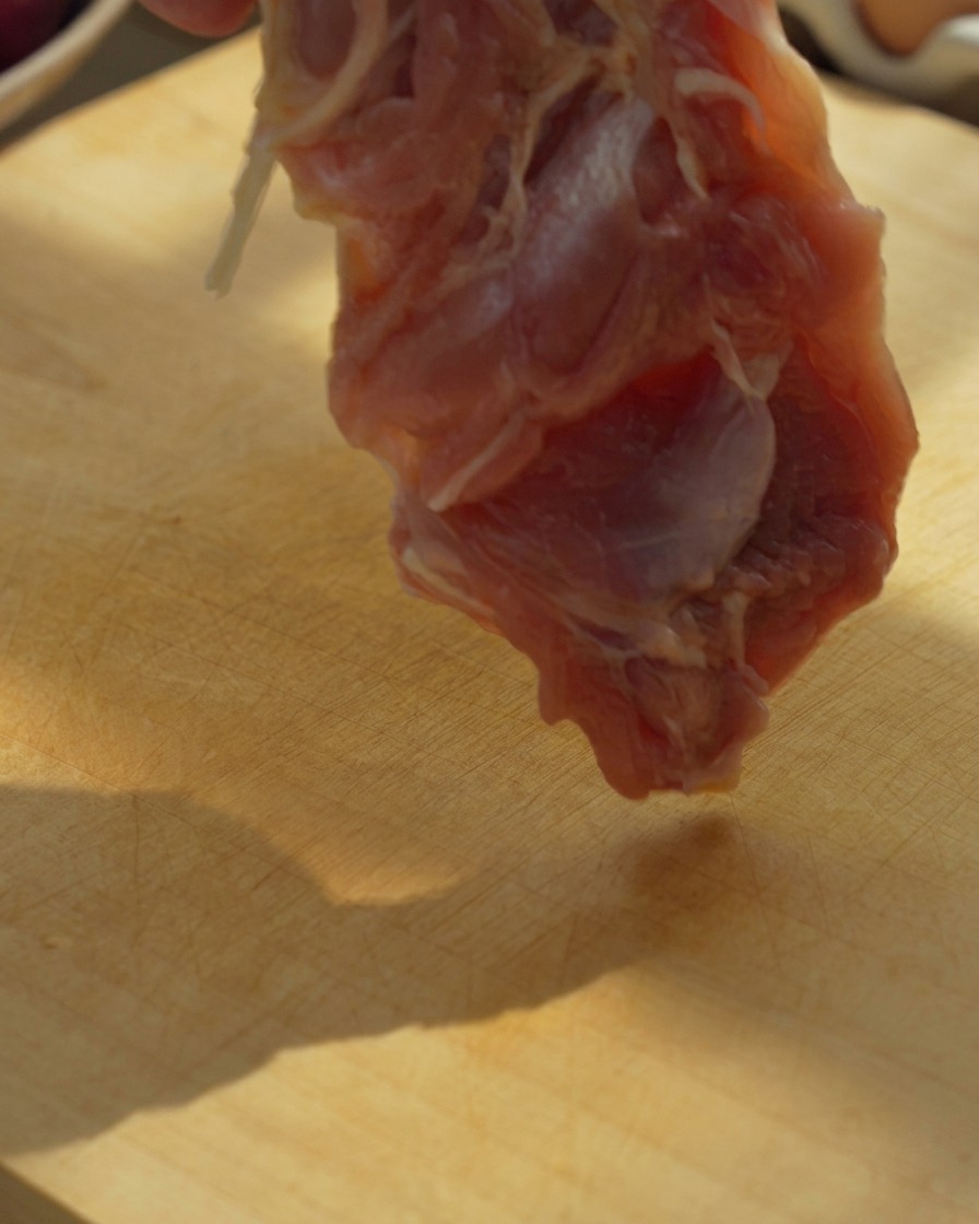 Filetti di coscia di pollo disossati tagliati a pezzi grandi su un tagliere di legno con un coltello.