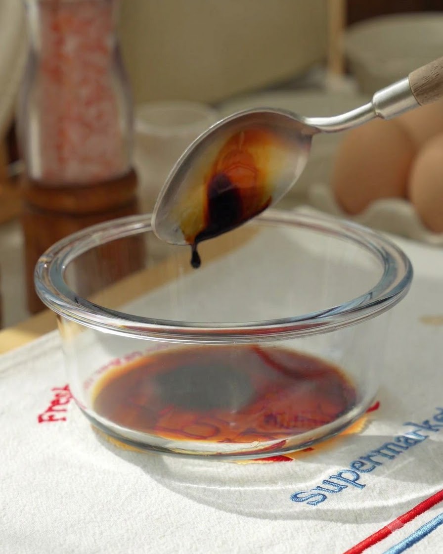 Salsa di soia versata da un cucchiaio in una ciotola di vetro contenente gli ingredienti della salsa.
