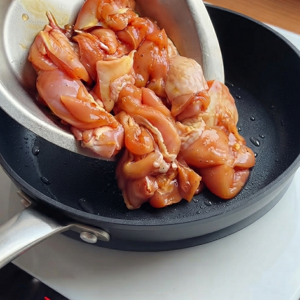 Bocconcini di pollo marinati versati da una ciotola in una padella nera calda.