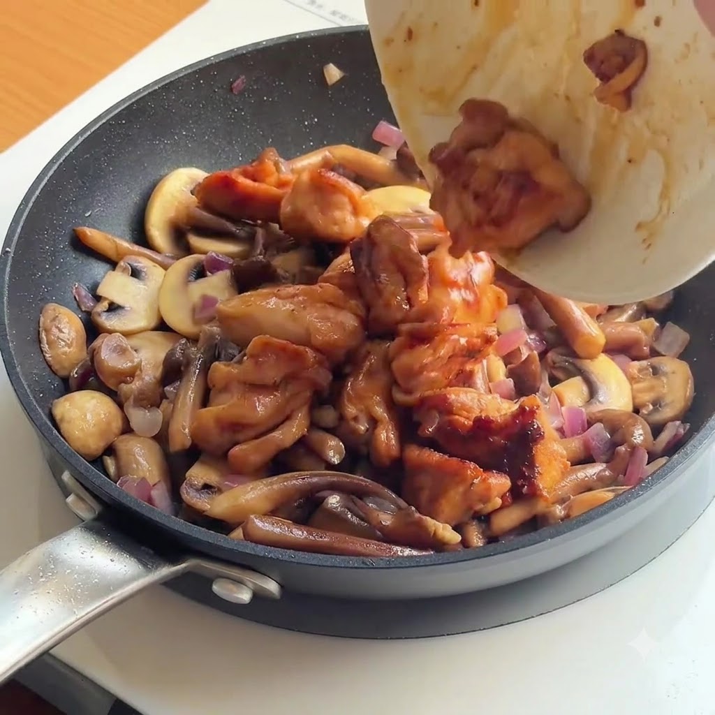 Pollo cotto e riso bianco versati in una padella piena di funghi e cipolle saltati.