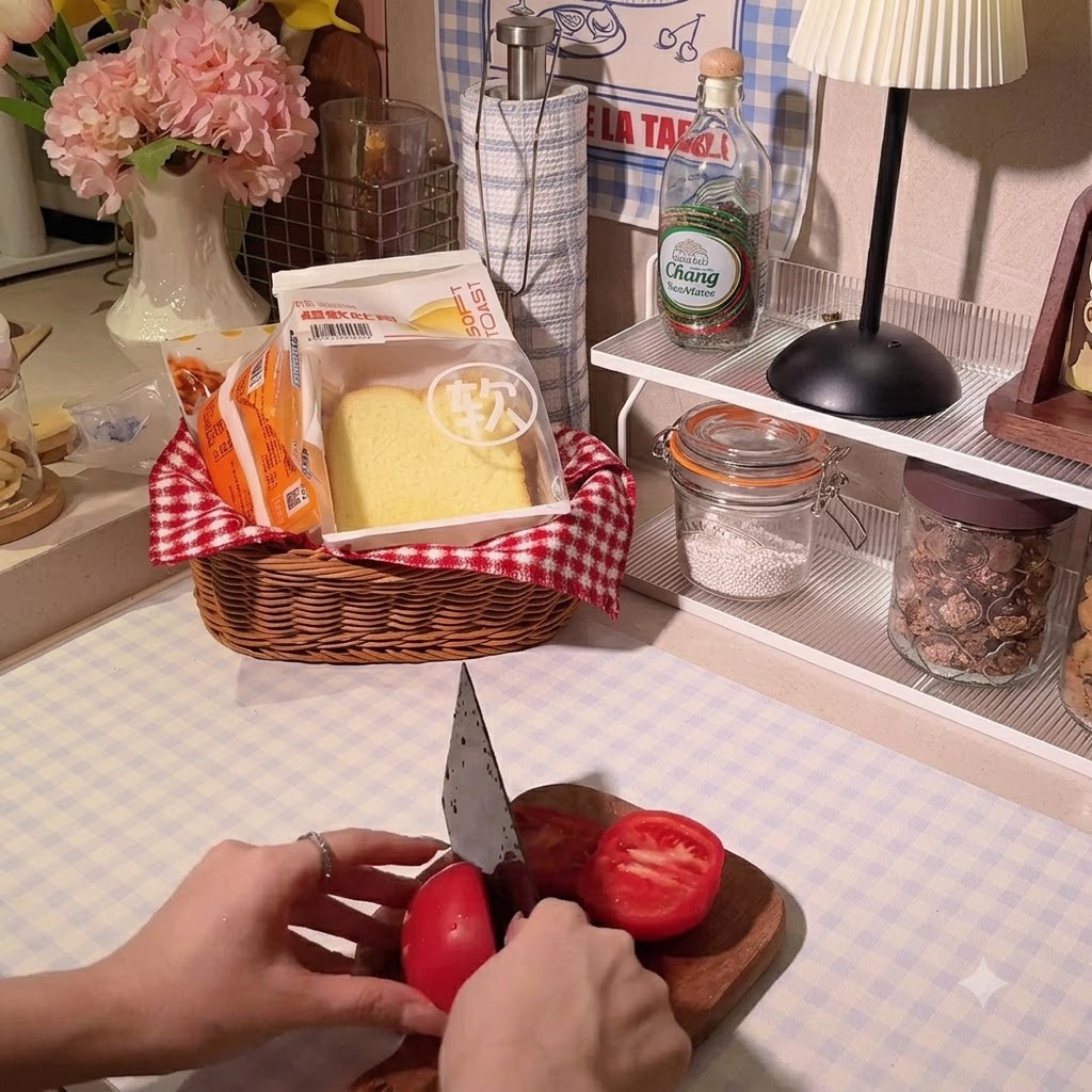 Le mani di una persona che usano un coltello da chef per affettare un pomodoro rosso vivo su un tagliere di legno.