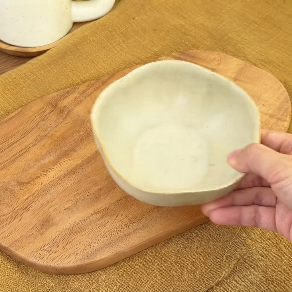 Una ciotola di ceramica vuota tenuta sopra un tagliere di legno pronta per mescolare la salsa.