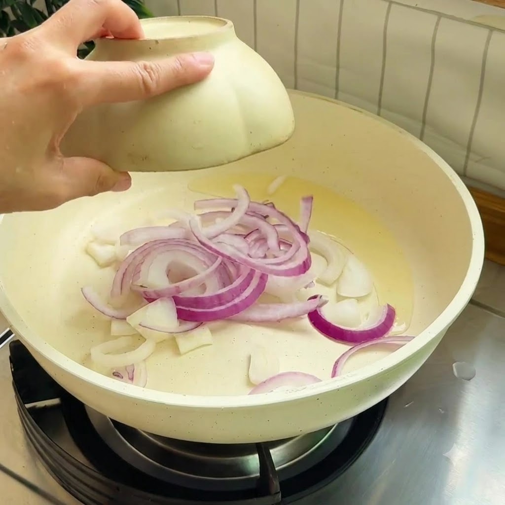 Strisce di cipolla rossa che soffriggono in una padella calda con olio da cucina.