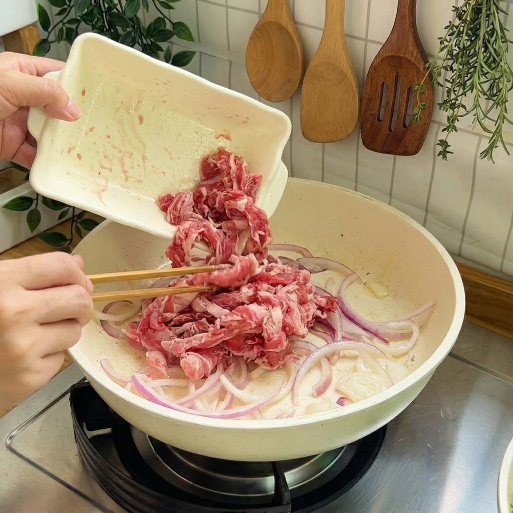 Fettine di manzo crudo aggiunte alla padella con le cipolle per la cottura saltata.