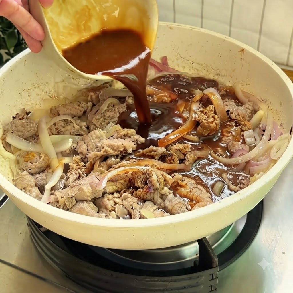 Salsa marrone ricca versata da una piccola ciotola in una padella bianca contenente manzo e cipolle affettate.