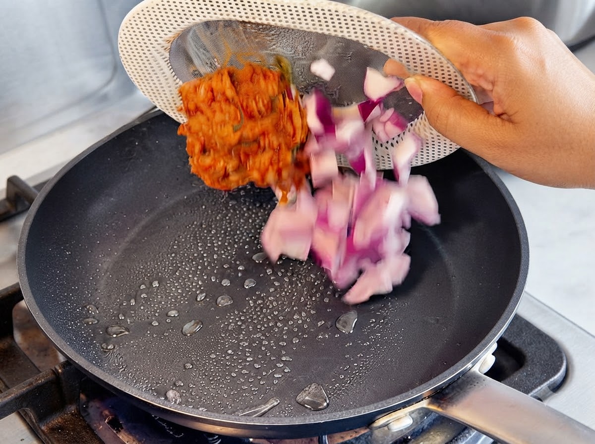 Cipolle viola tritate e kimchi rosso versati da un piatto scolapasta in una padella calda con gocce dolio.