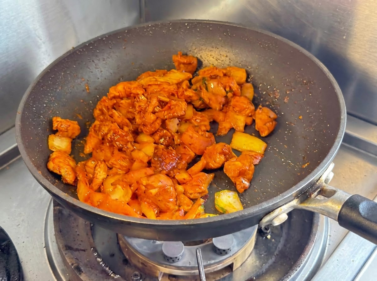 Petto di pollo a dadini, cipolle e kimchi tritato saltati insieme in una padella antiaderente scura.