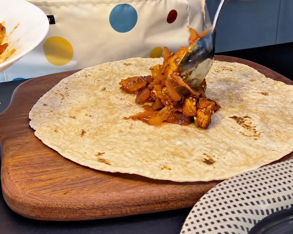 Un grande cucchiaio di ripieno piccante di pollo e kimchi posizionato al centro di una tortilla integrale.