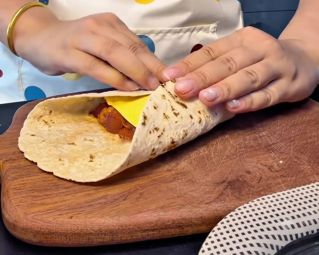 Mani che piegano strettamente i bordi di una piadina sopra una fetta di formaggio e il ripieno per creare un pacchetto quadrato sigillato.