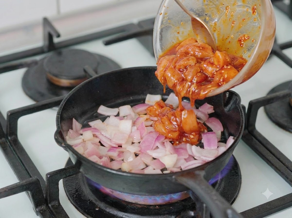 Pezzi di pollo marinato versati da una ciotola in una padella contenente cipolle tritate.