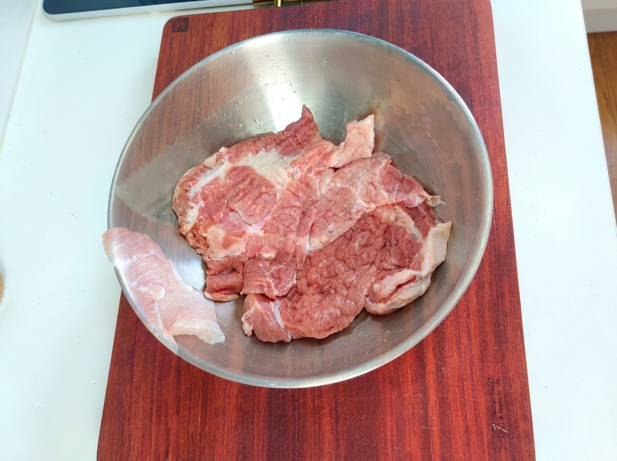 Pezzi di maiale in una ciotola di metallo con gli ingredienti della marinata.