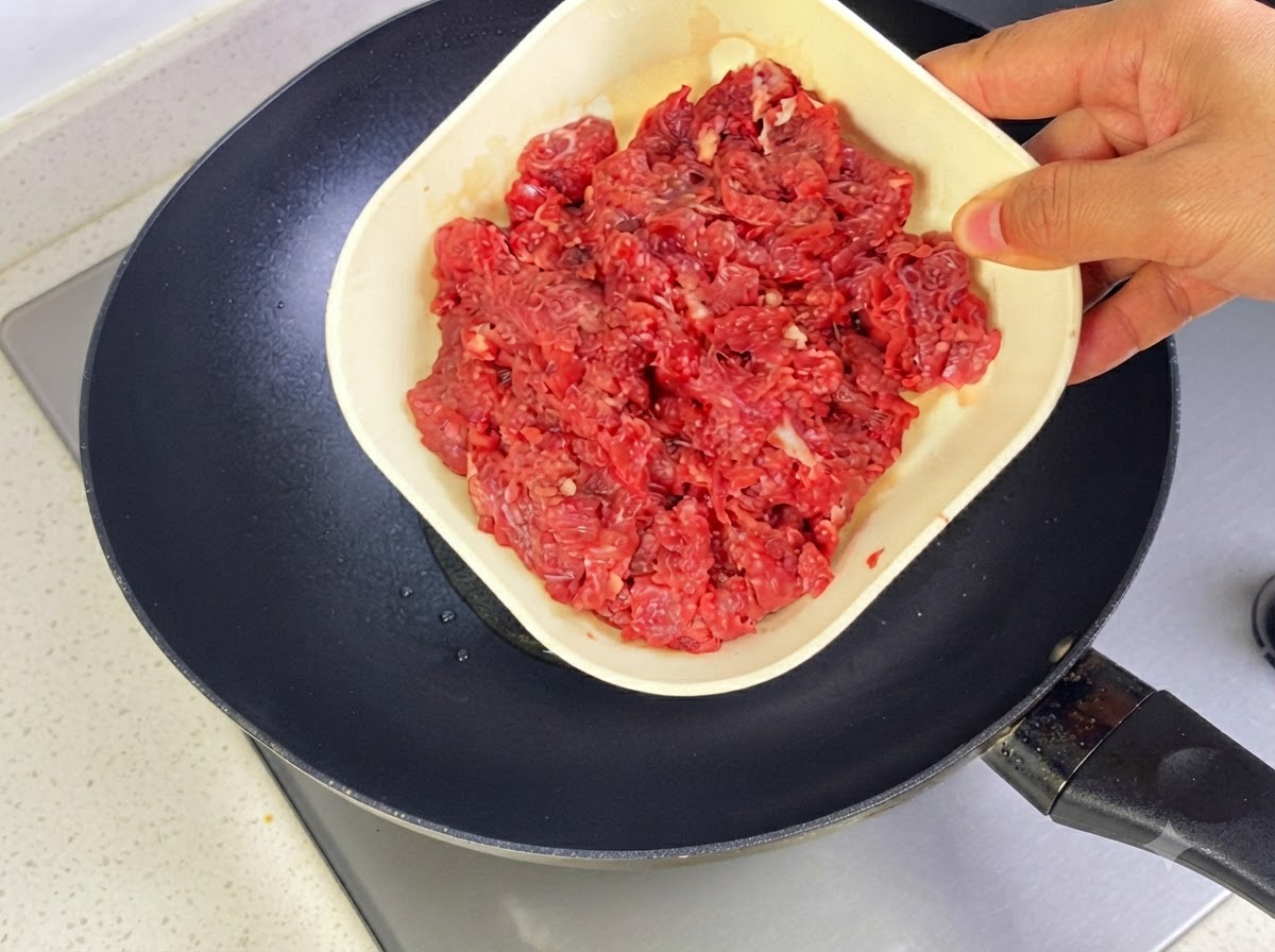 Carne macinata di manzo aggiunta a una padella calda con olio per soffriggere.