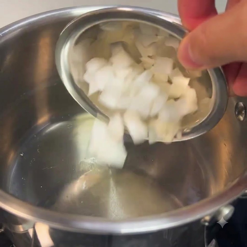 Cipolle bianche tritate versate da una ciotola in una pentola di acciaio inossidabile.