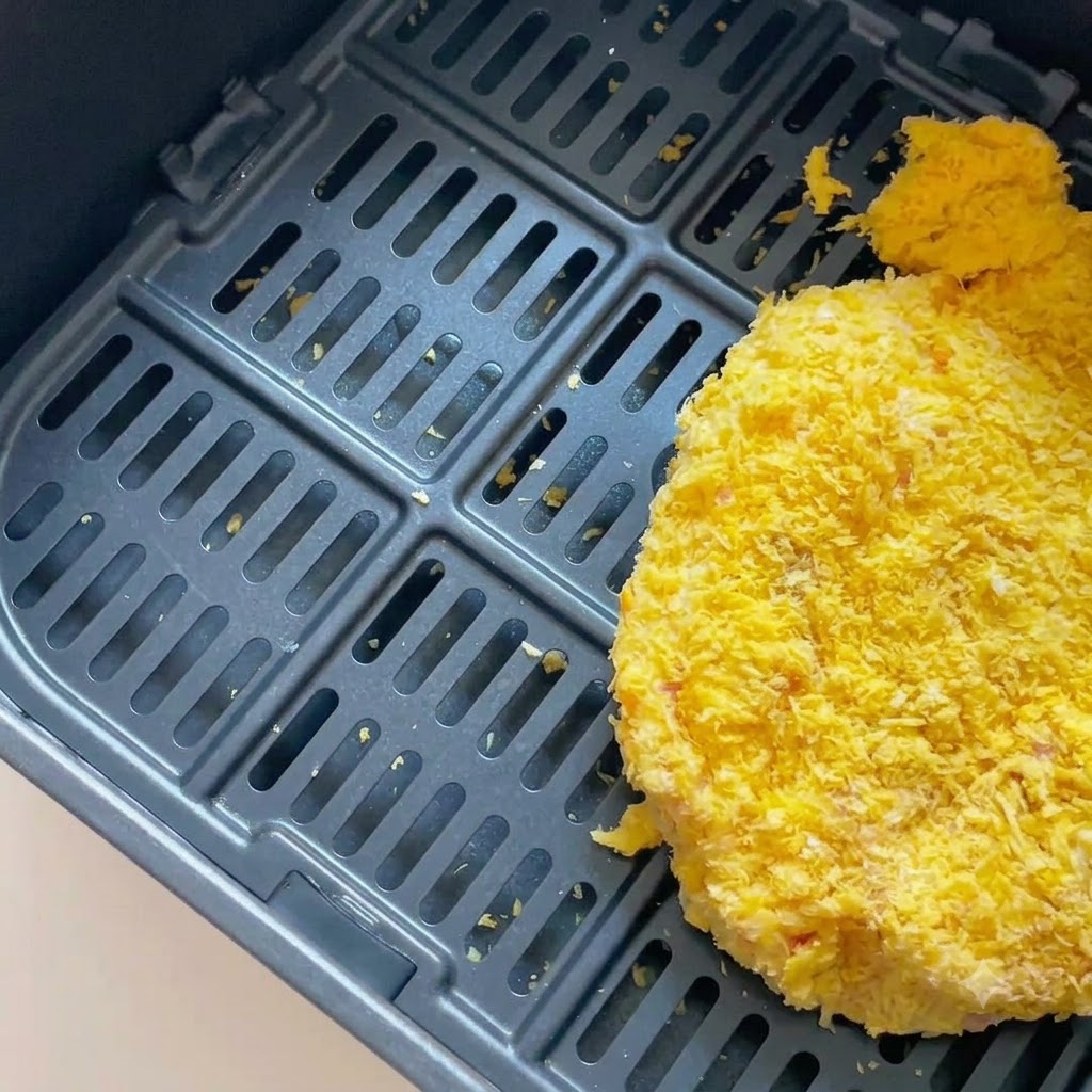 Una cotoletta di maiale impanata allinterno del cestello scuro della friggitrice ad aria.