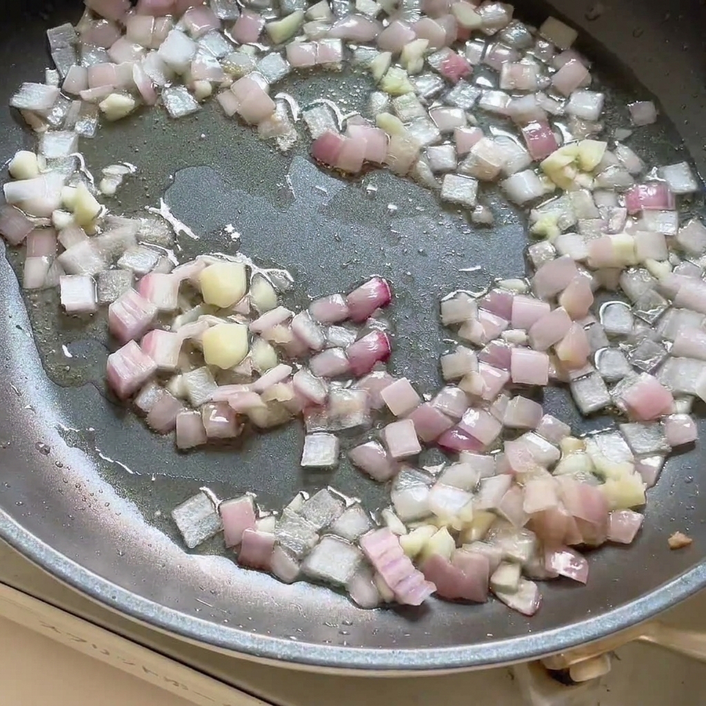 Pasta di curry aggiunta alla padella con cipolle e aglio saltati, mescolata insieme.