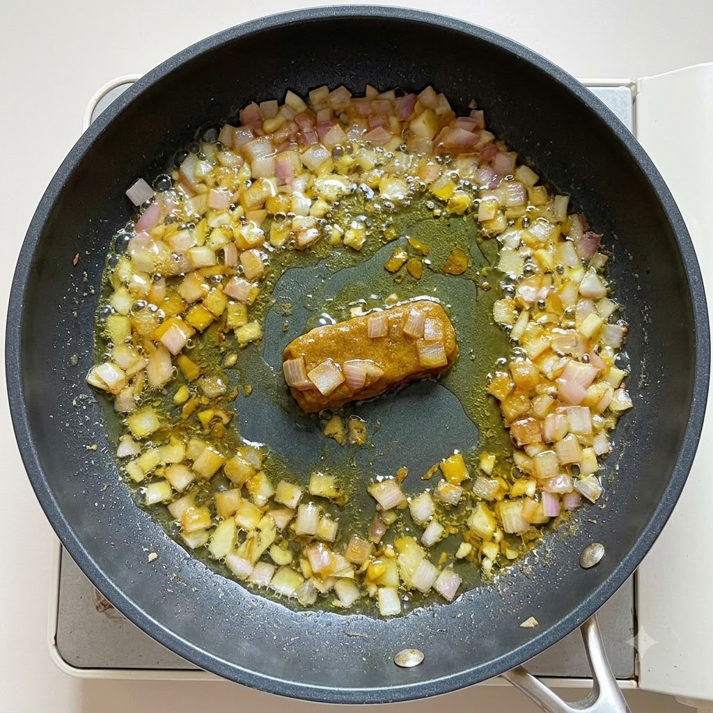 Acqua e latte di cocco versati nella base di curry in padella, mescolati fino a ottenere una consistenza densa.