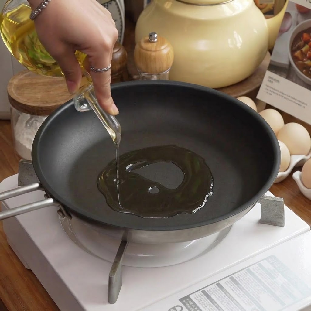 Olio versato in una padella sul fuoco accanto a uova e utensili da cucina.