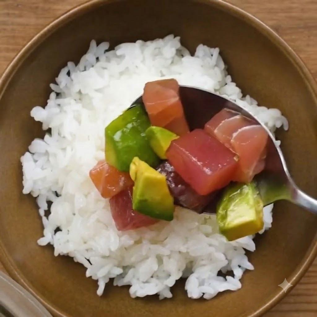 Un cucchiaio pieno di tonno e avocado marinati posizionato sopra una ciotola di riso bianco per sushi.