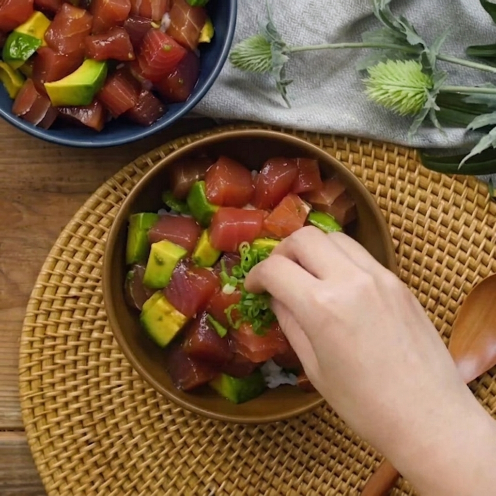 Una mano che cosparge cipollotti tritati sopra la ciotola di tonno e avocado.