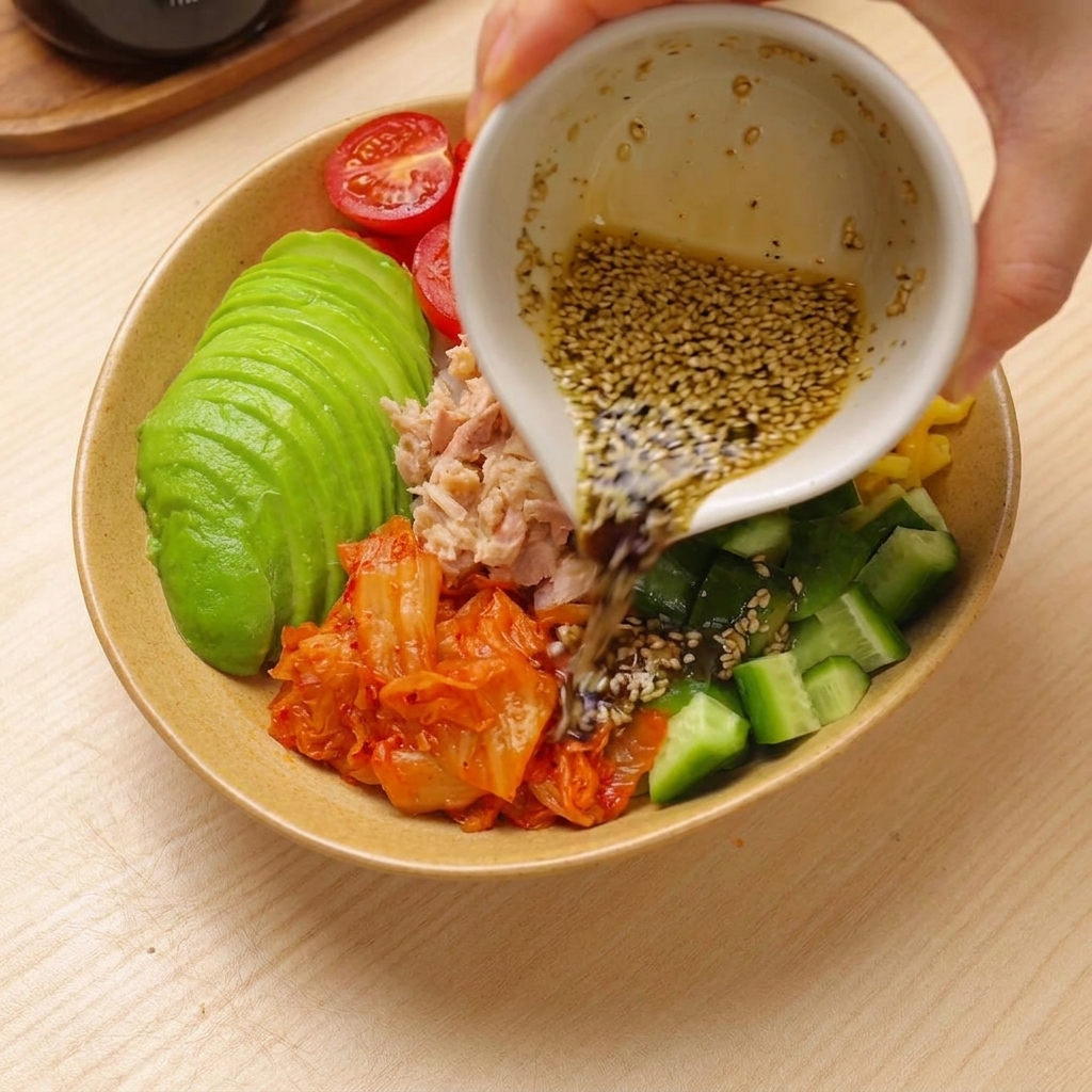 Il condimento che viene versato su una colorata bowl di riso con tonno e avocado assemblata.
