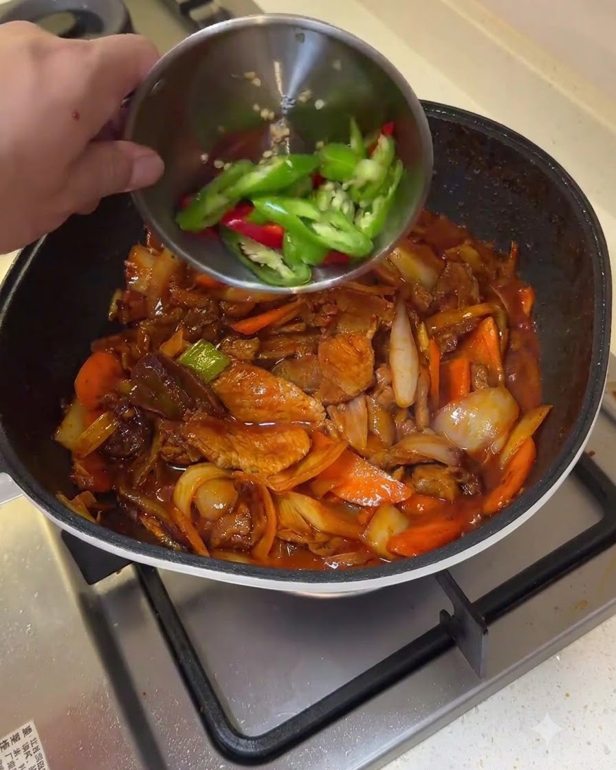 Fette di peperoncino verde e rosso versate da una ciotolina in una padella di maiale saltato e verdure.