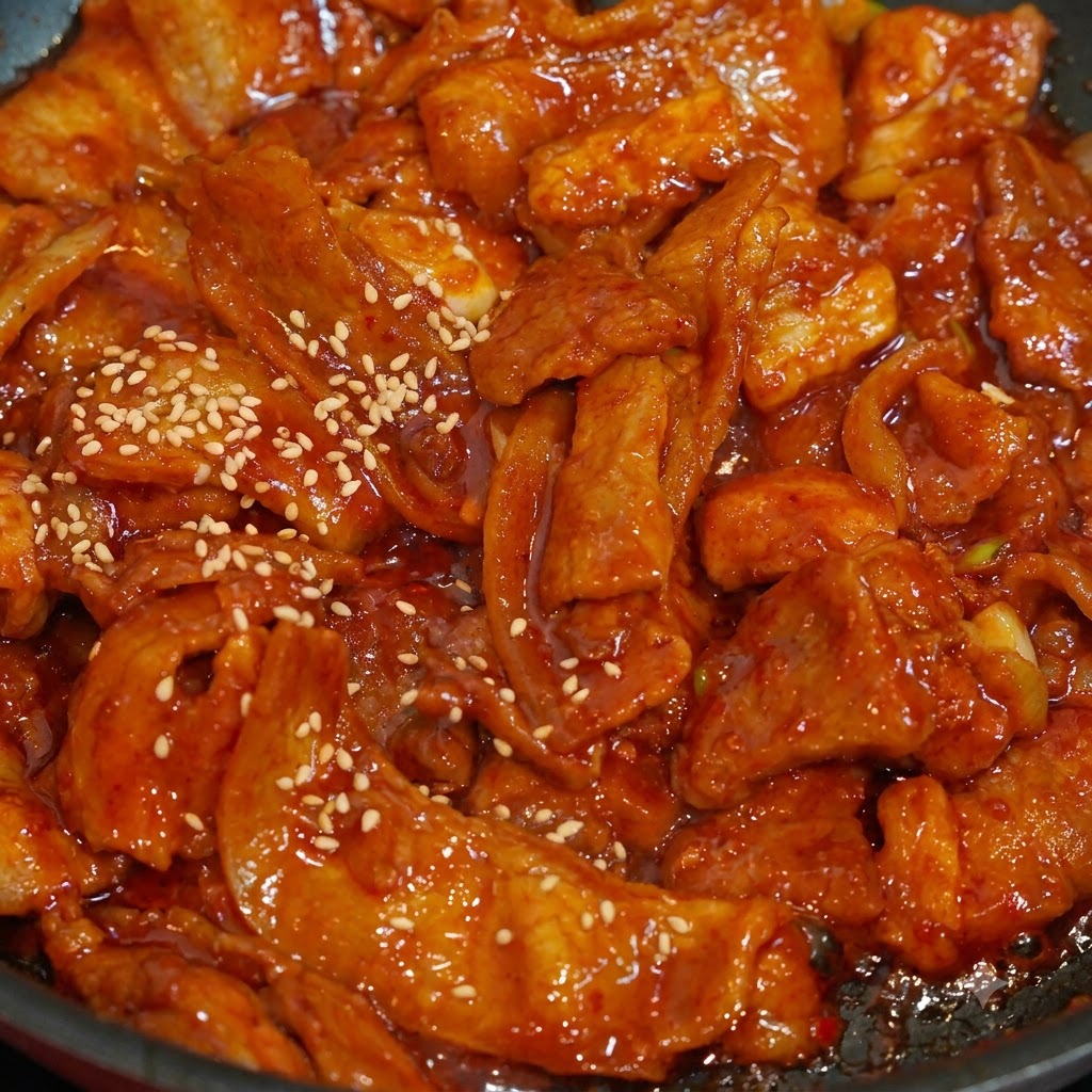 Primo piano di semi di sesamo bianco cosparsi sulle fette di maiale piccante rosso e succoso in una padella.