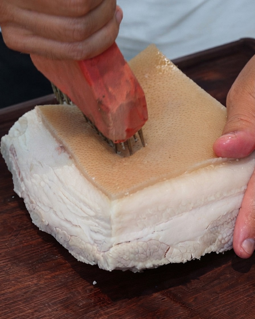 Primo piano di uno strumento per forare la carne che fora ripetutamente la superficie della cotenna di maiale.