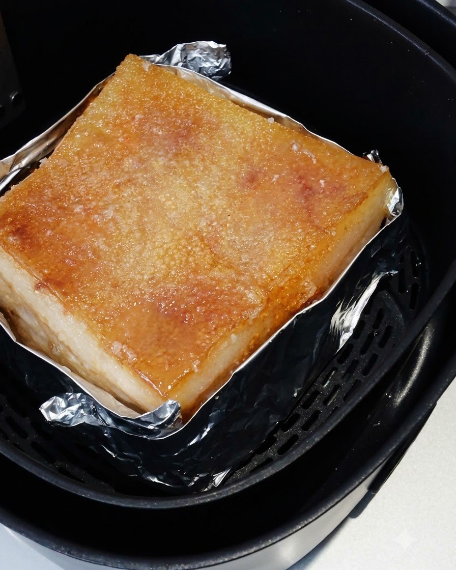 La pancetta di maiale arrosto allinterno del cestello della friggitrice ad aria con la pelle salata cotta a tonalità dorata.