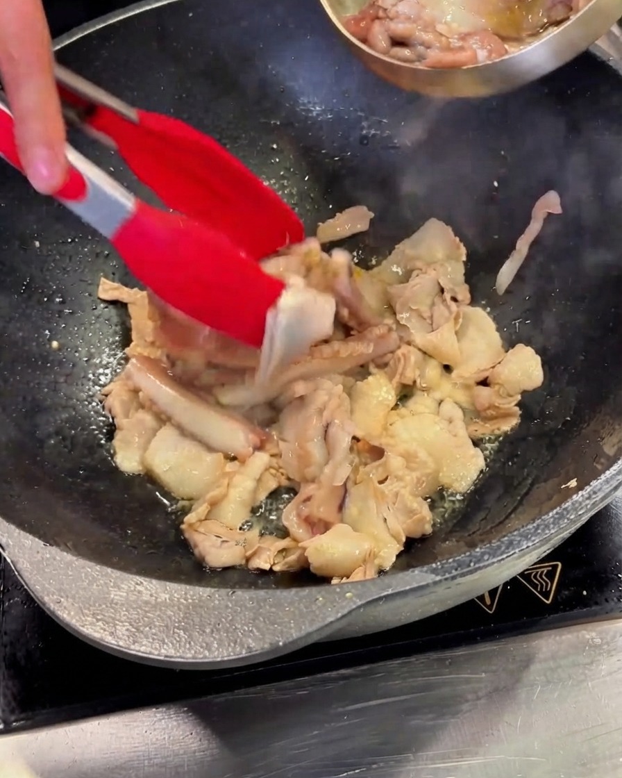 Pezzi di totano puliti versati da una ciotola dacciaio nel wok contenente la pancetta di maiale.