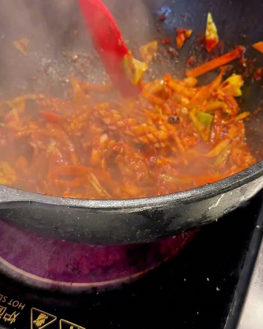 Una spatola rossa che mescola il composto sfrigolante nel wok a fiamma viva.