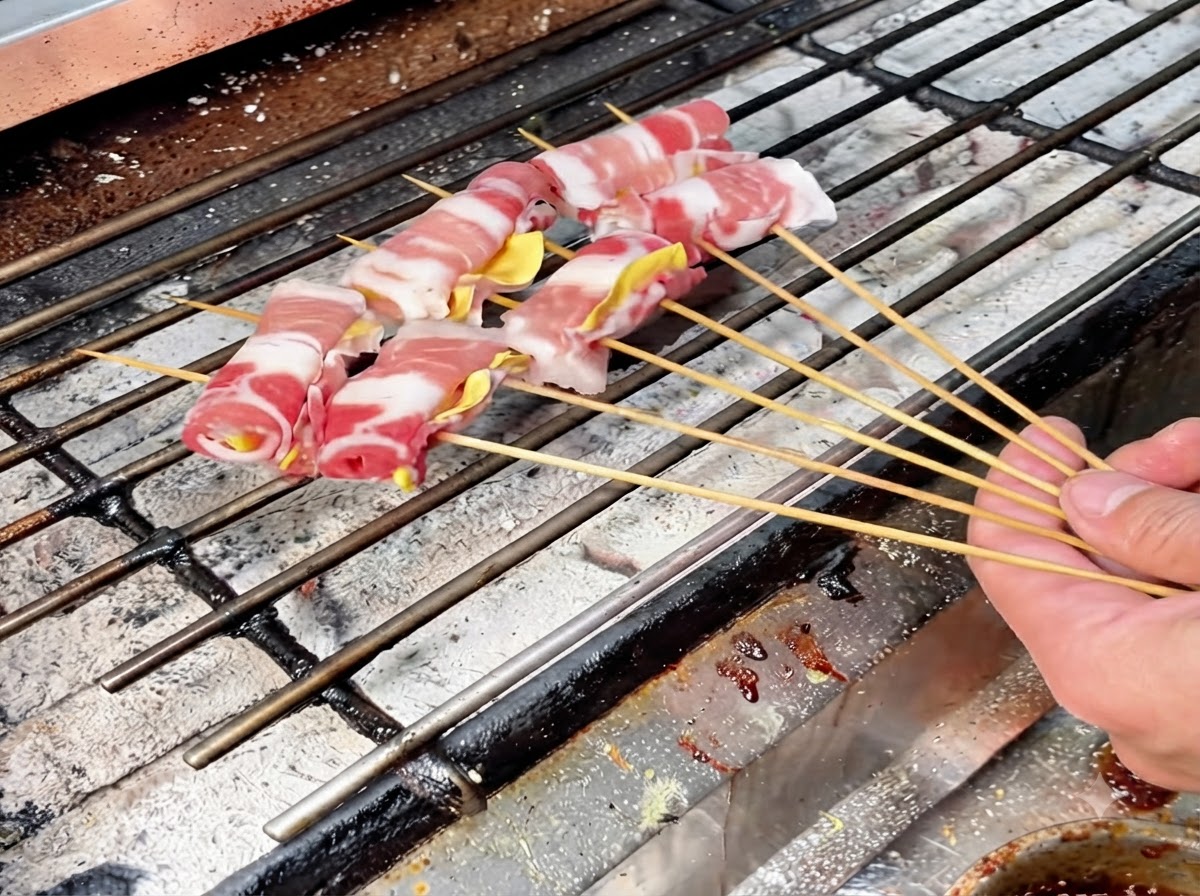Diversi involtini di carne infilzati disposti su una griglia a carbone calda per la cottura lenta.