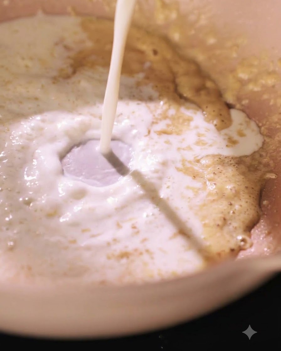 Latte che viene versato in una padella con una miscela di roux, creando un vortice.