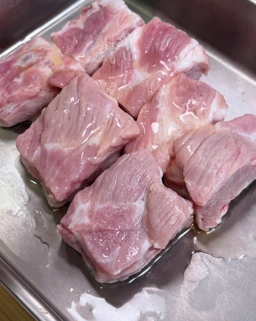 Costine di maiale in un vassoio di metallo condite con salse di soia, salsa di ostriche e pepe.